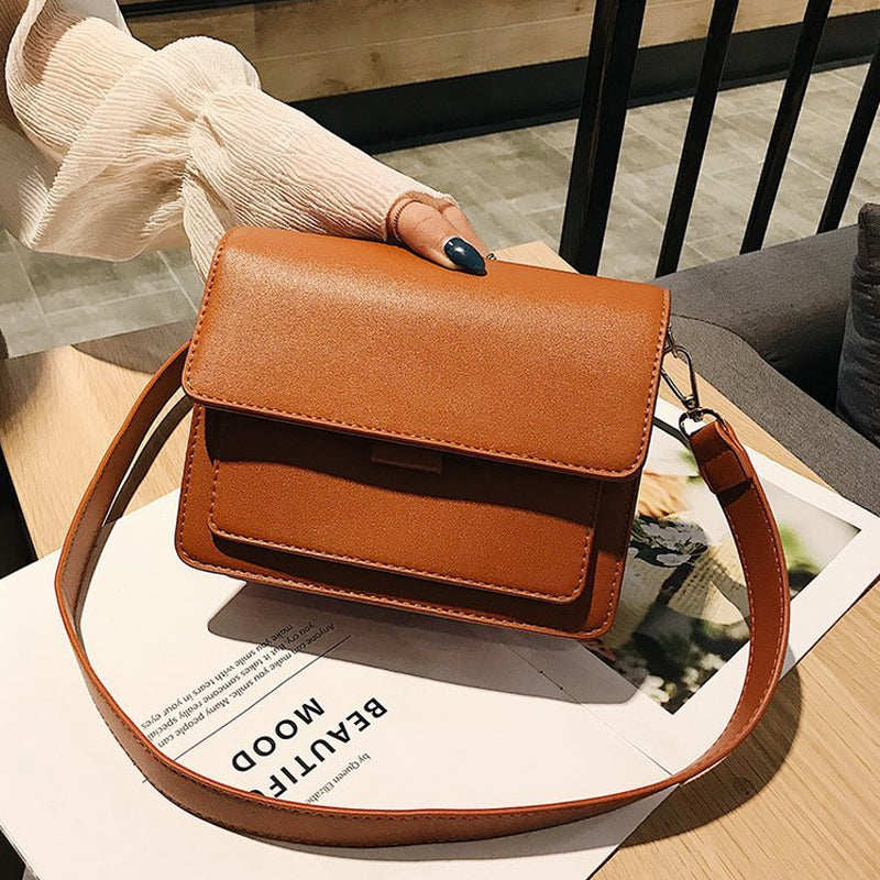 Svart retro crossbody väska i konstläder med minimalistisk design och flera fack för damaccessoarer.