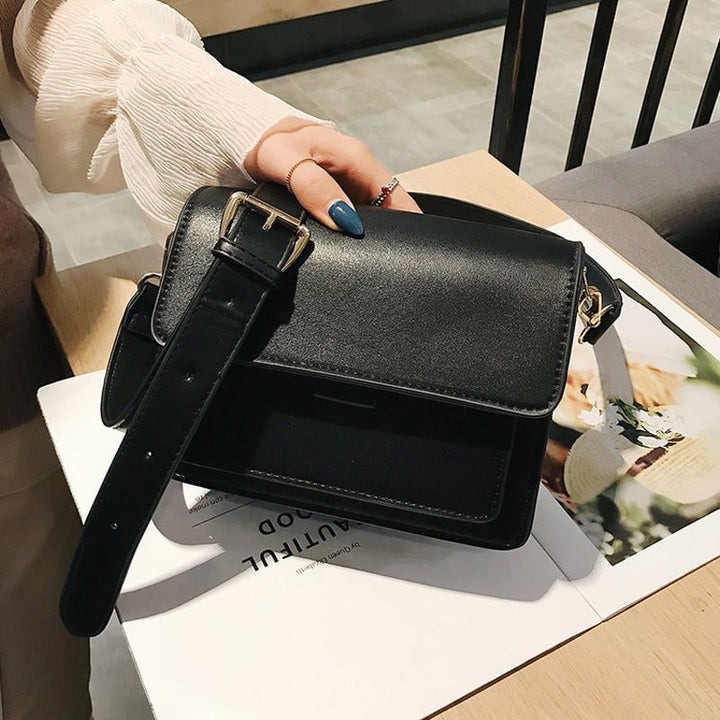 Svart retro crossbody väska i konstläder med minimalistisk design och flera fack för damaccessoarer.