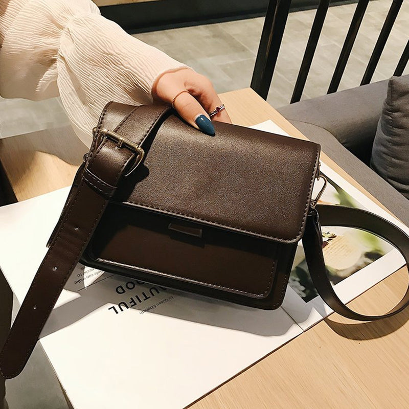 Svart retro crossbody väska i konstläder med minimalistisk design och flera fack för damaccessoarer.