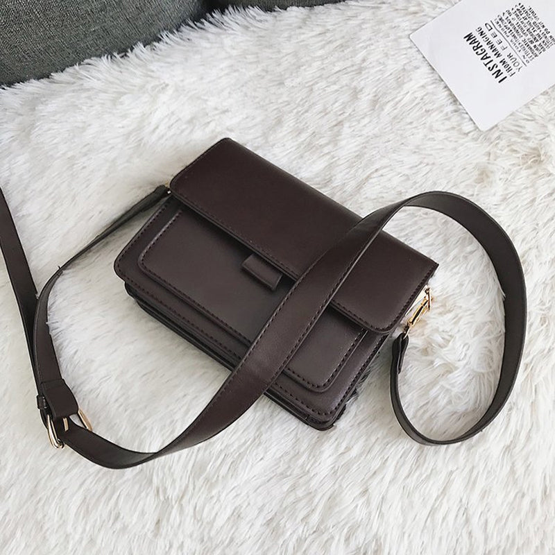 Svart retro crossbody väska i konstläder med minimalistisk design och flera fack för damaccessoarer.