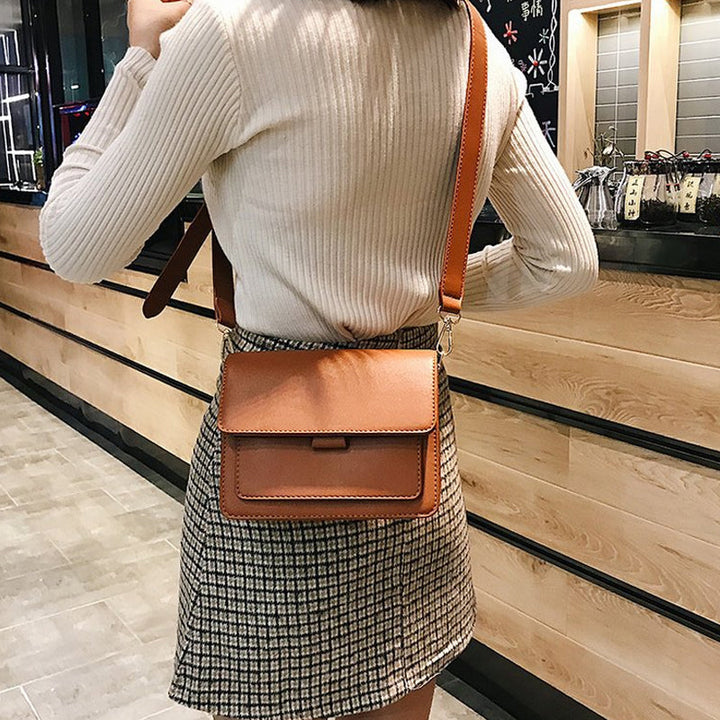Svart retro crossbody väska i konstläder med minimalistisk design och flera fack för damaccessoarer.