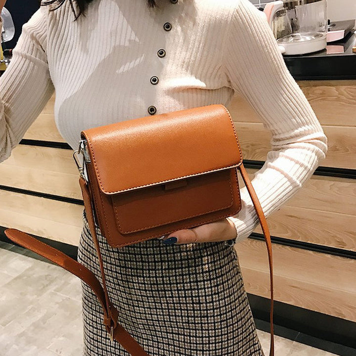 Svart retro crossbody väska i konstläder med minimalistisk design och flera fack för damaccessoarer.
