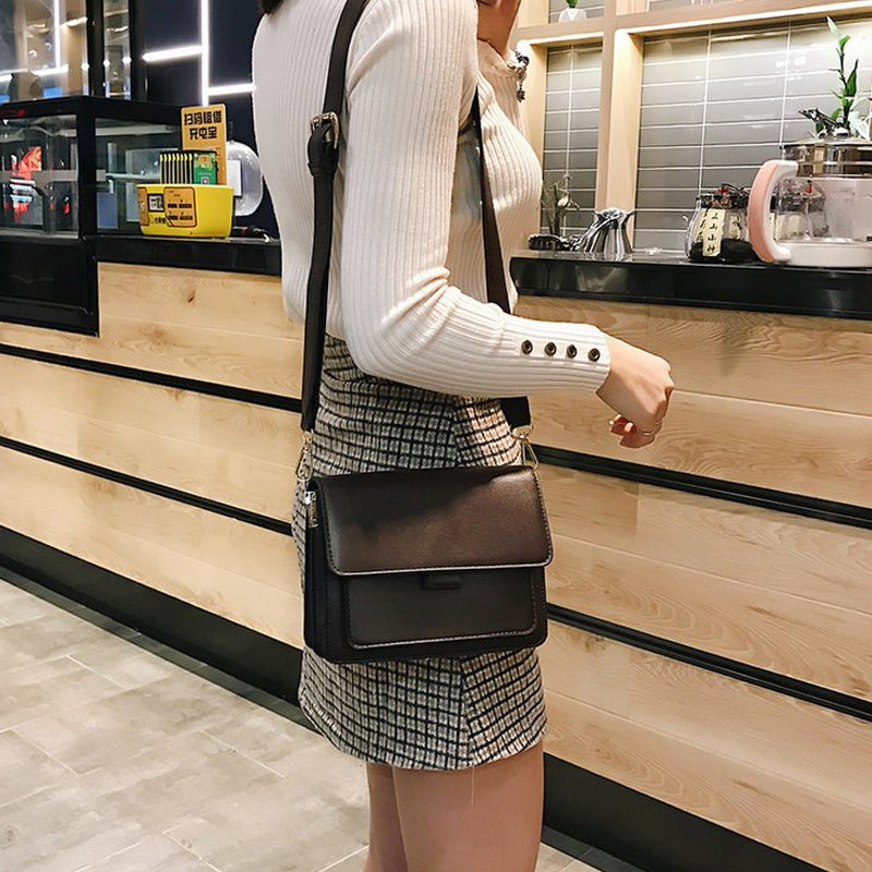 Svart retro crossbody väska i konstläder med minimalistisk design och flera fack för damaccessoarer.