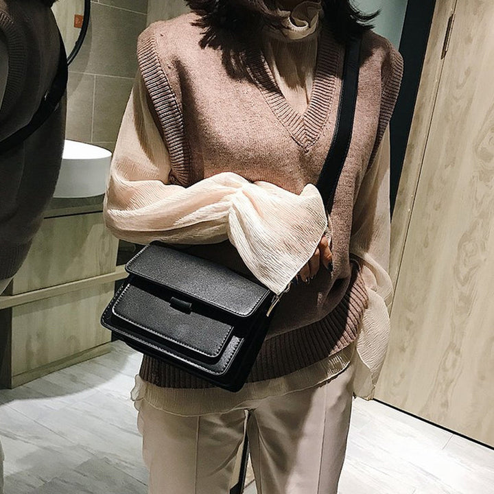 Svart retro crossbody väska i konstläder med minimalistisk design och flera fack för damaccessoarer.