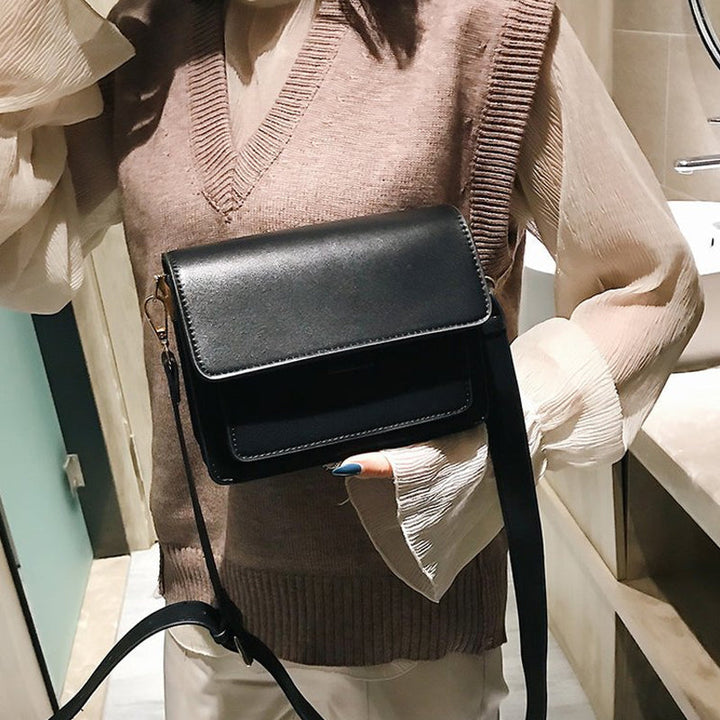 Svart retro crossbody väska i konstläder med minimalistisk design och flera fack för damaccessoarer.
