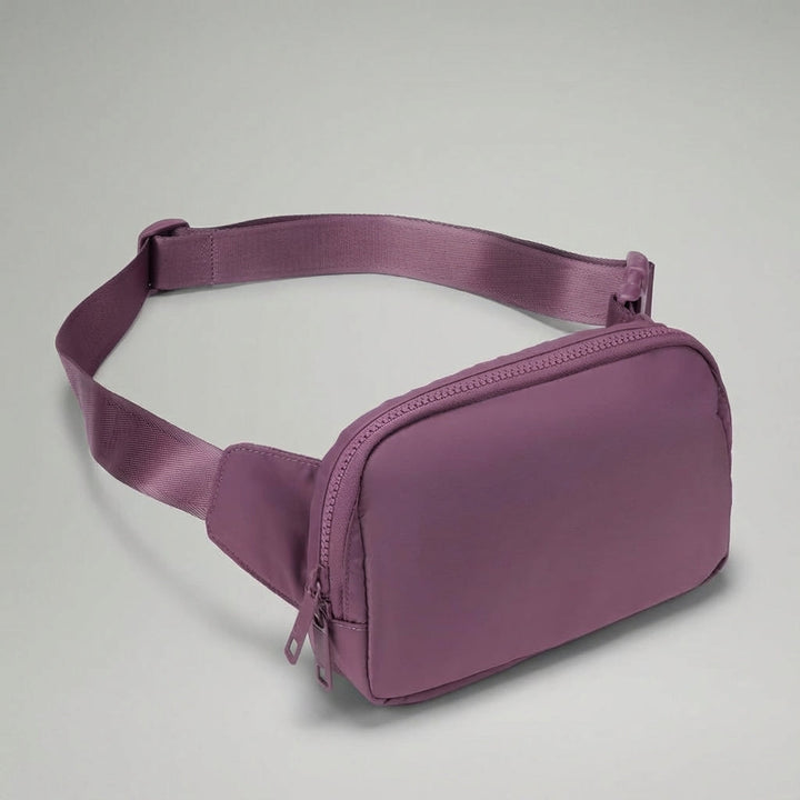 Lila organiserad midjeväska i nylon för resor. Kompakt och säker för dina viktigaste tillhörigheter. Unisex modell.