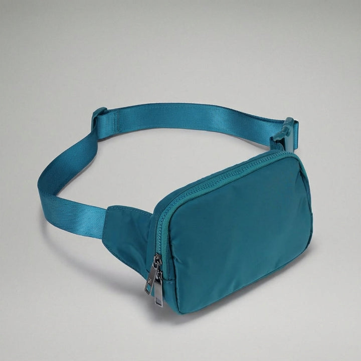 Grå kompakt unisex fannypack i nylon med flera fack, perfekt för att hålla ordning. Lätt att bära på resan.