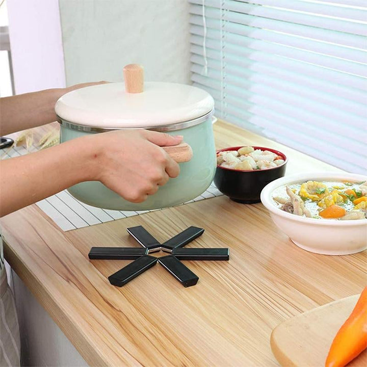 "Svart vikbar silikonplatta, värmeisolerande och halkfri, skyddar köksbord med stil. Perfekt för köks- och tallriksmattor."