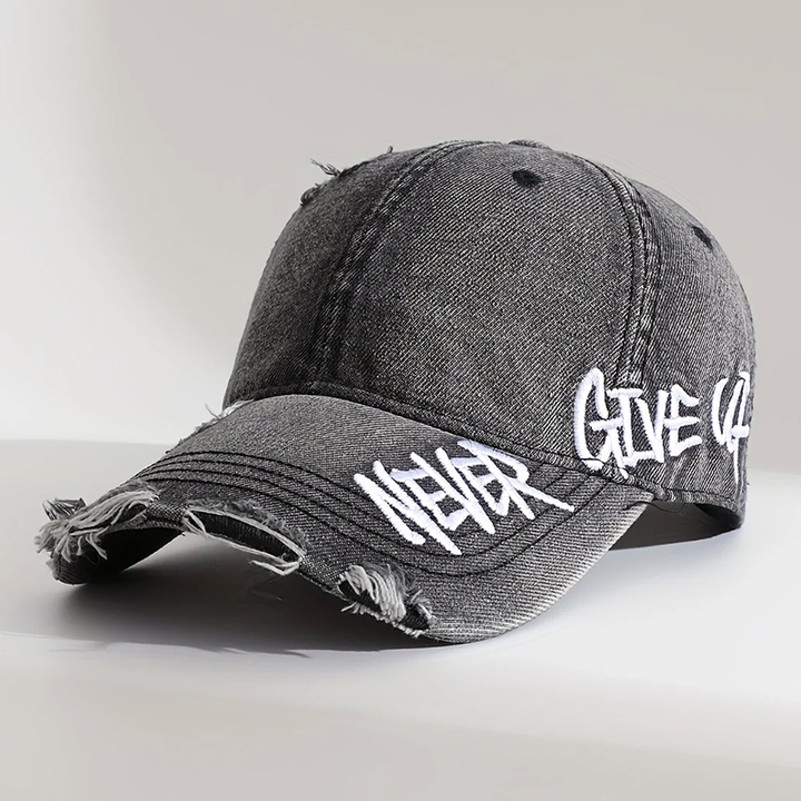 Närbild av en avslappnad baseballkeps i distressed denim med unikt broderi, justerbar och unisex.