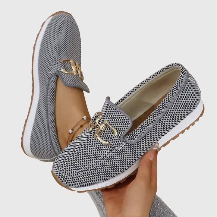 En kvinna som provar avslappnade sommarskor, beiga slip-on loafers, inomhus.